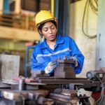 Woman worker in uniform operating machine at factory concentrate on fabrication job on lathe